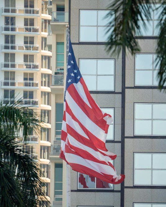 American flag waving in front of Miami skyline with buildings as backdrop