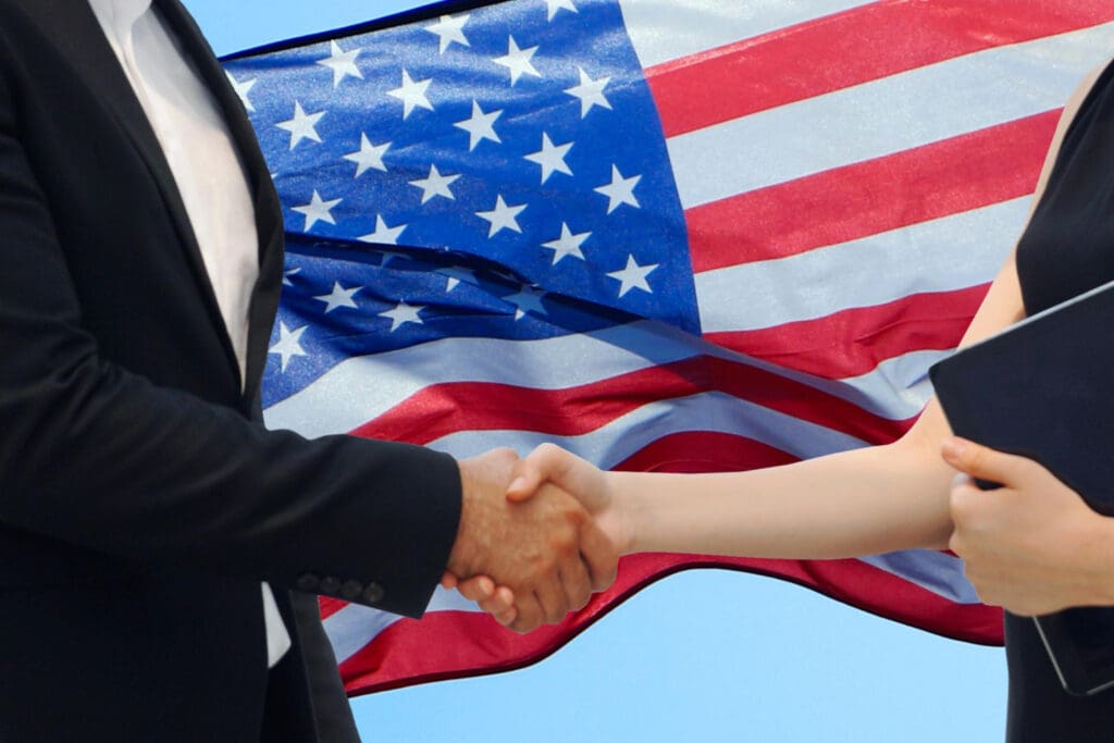 A low-angle view of a handshake with the USA flag in the background against a clear blue sky