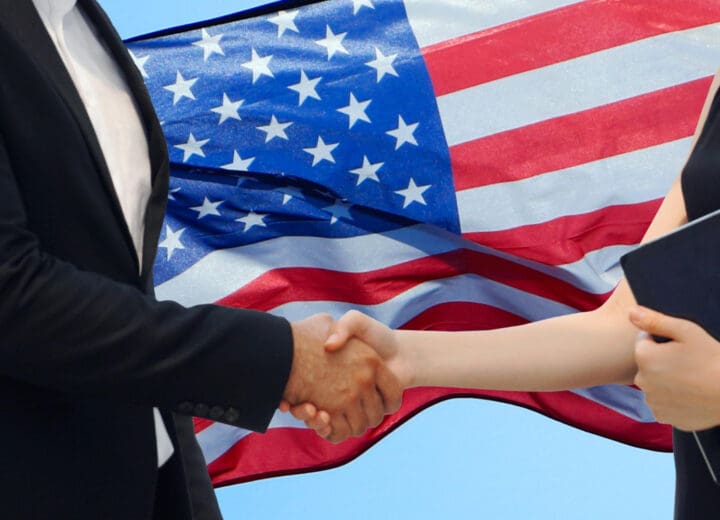 A low-angle view of a handshake with the USA flag in the background against a clear blue sky